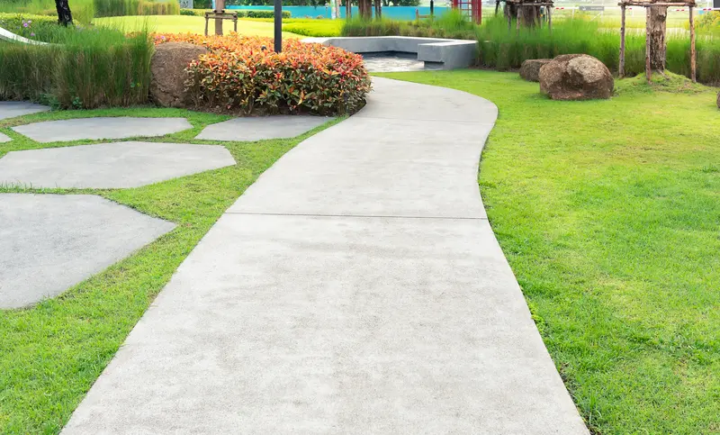 Modern curved concrete walkway winding through a beautifully landscaped green garden.