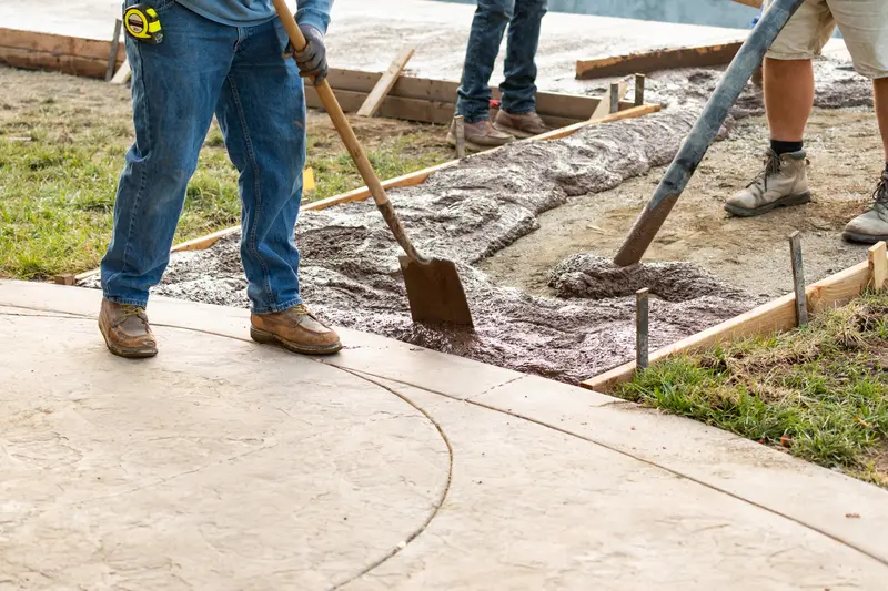 Concrete patio installation with workers spreading wet concrete using a shovel. Concrete patio installation with workers spreading wet concrete using a shovel.
