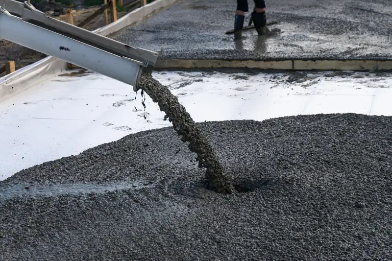 Fresh liquid concrete pouring from mixer chute during patio installation Fresh liquid concrete pouring from mixer chute during patio installation