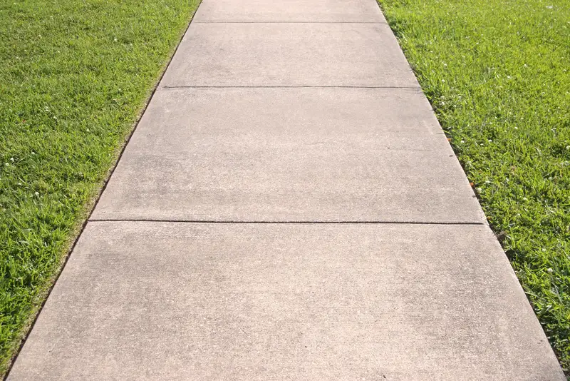 Finished concrete sidewalk path surrounded by green lawn. Finished concrete sidewalk path surrounded by green lawn.