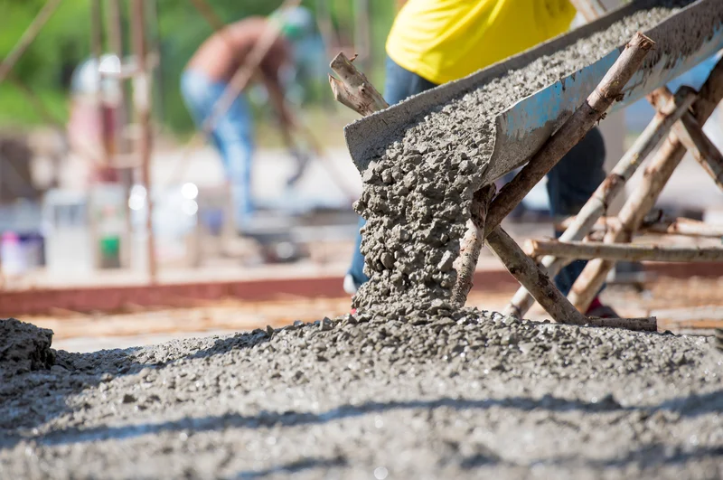 Fresh wet concrete mixture pouring from a chute onto a foundation. Fresh wet concrete mixture pouring from a chute onto a foundation.