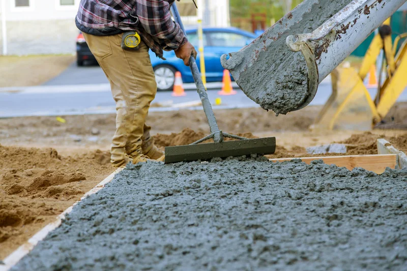 Construction worker using a concrete rake to spread wet cement from a chute. Construction worker using a concrete rake to spread wet cement from a chute.